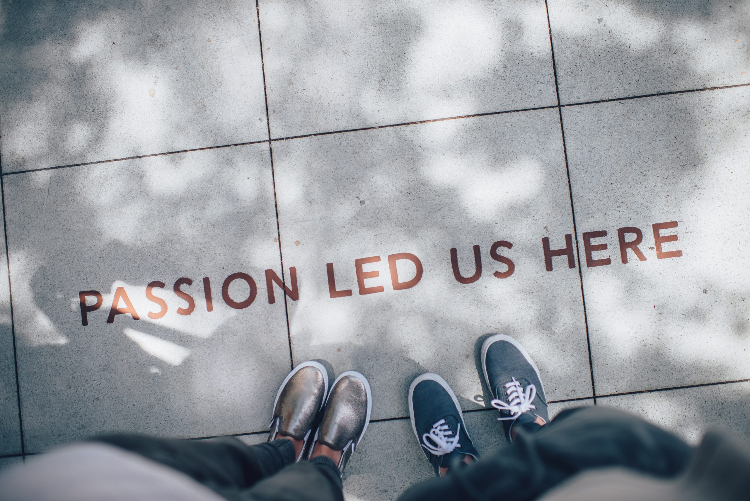 two pair of feet standing next to a sign that reads passion led us here