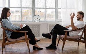man in black pants and-black-shoes-sitting-brown-chair talking with
