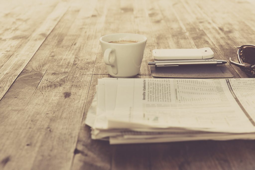 folded newspaper on wooden table beside coffee cup and cellphone