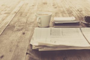 folded newspaper on wooden table beside coffee cup and cellphone
