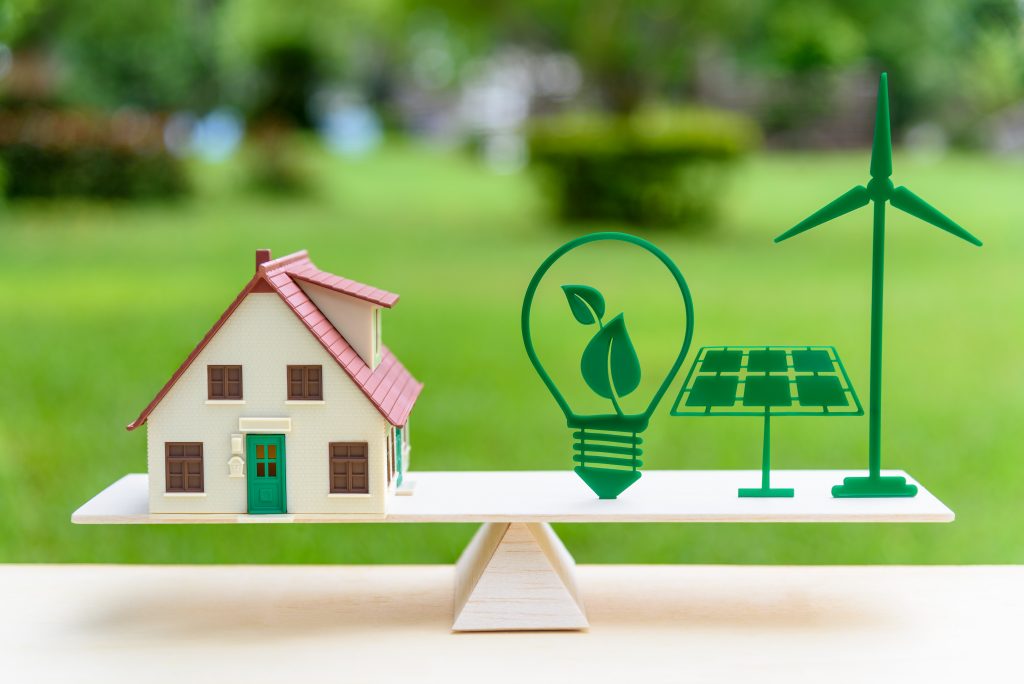  House model, light bulb with green leaf, solar panel, wind mill on wood balance scale, depicts the awareness of environment.