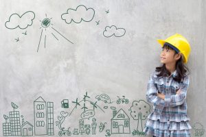 Little girl wearing construction hat against wall with cityscape drawn on it