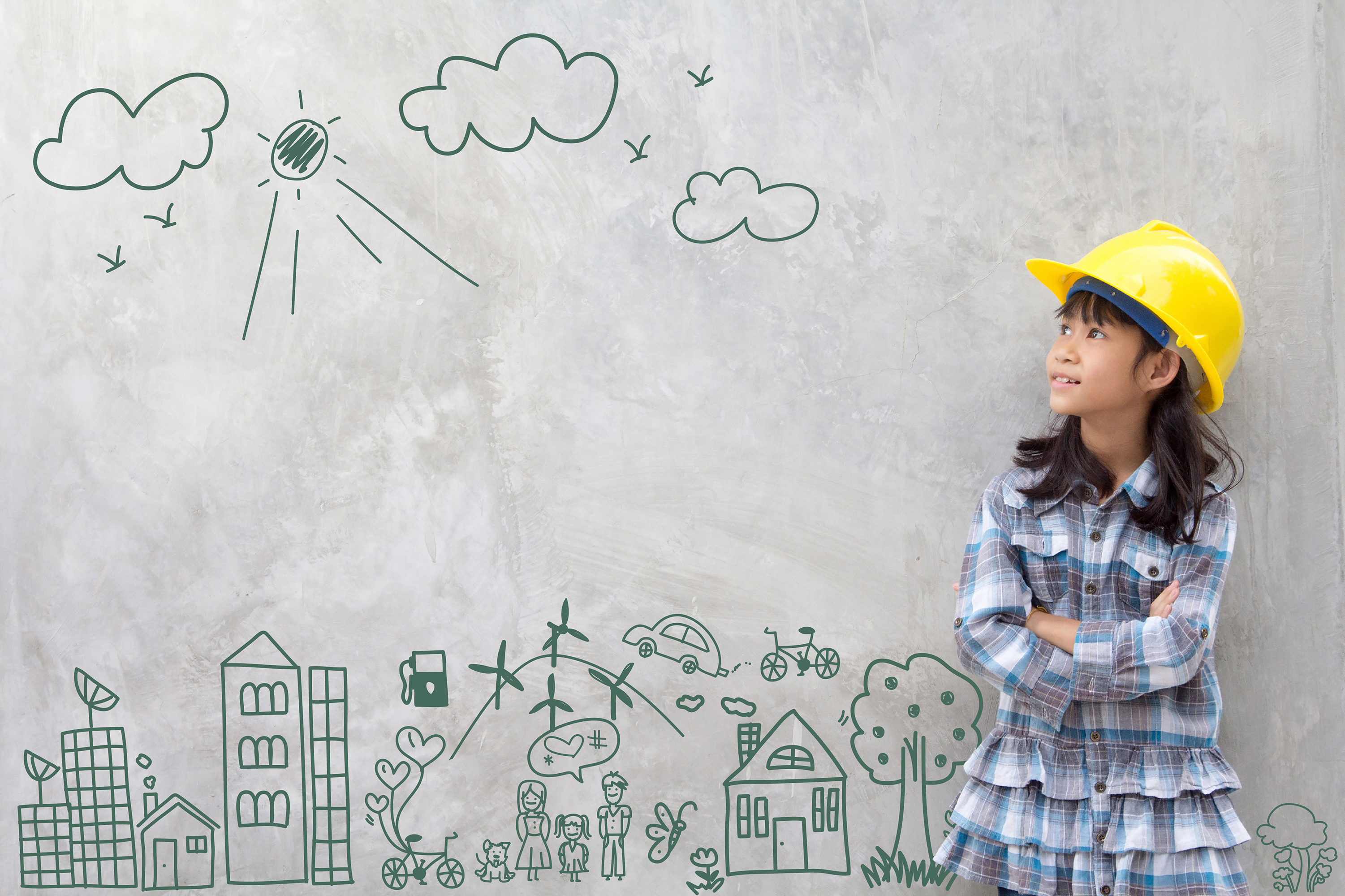 Little girl wearing construction hat against wall with cityscape drawn on it