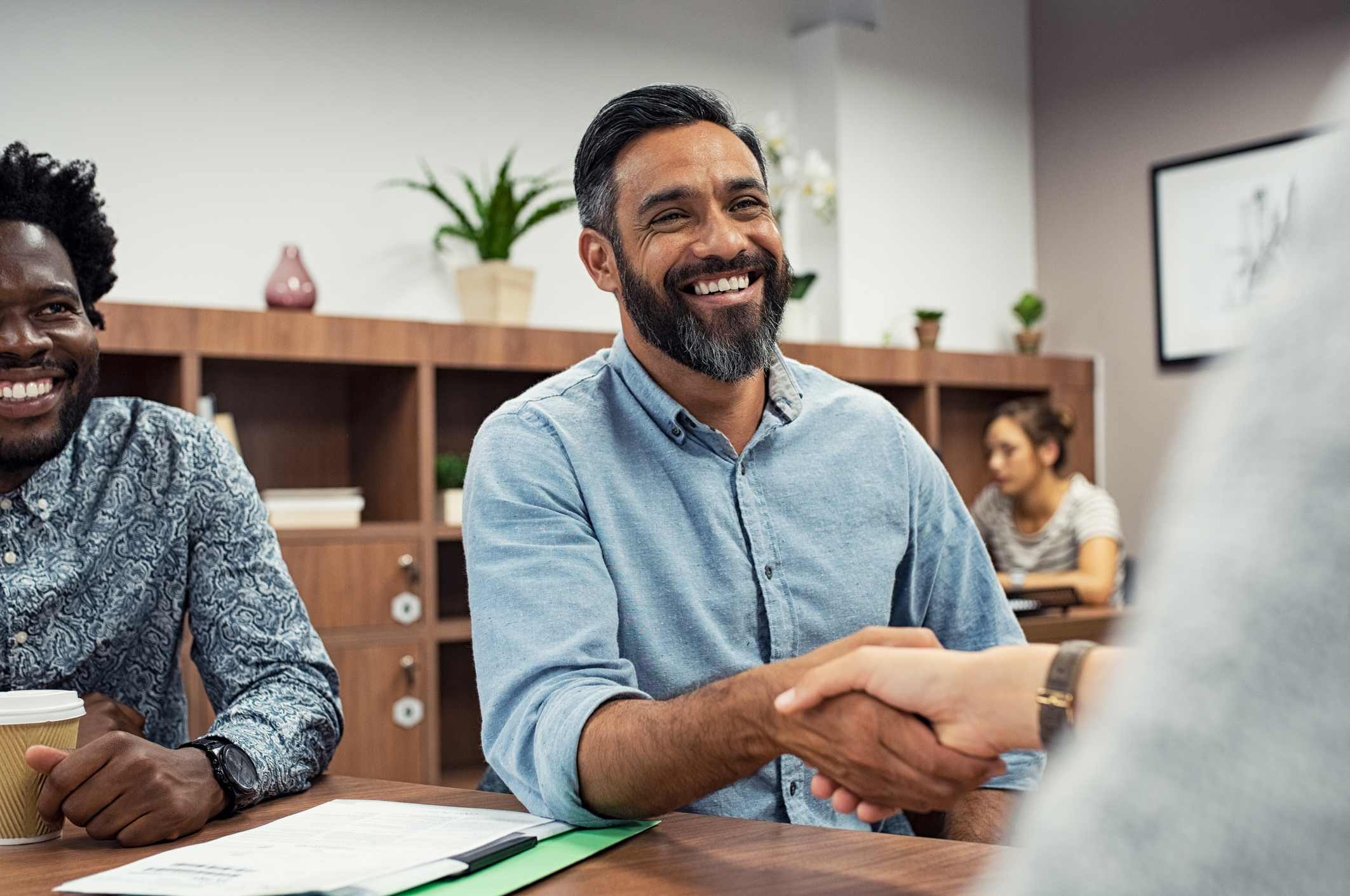 Two business people shaking hands while sitting in meeting room.