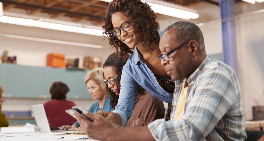 Woman Helping Retired Senior Man Attending IT Class In Community Centre