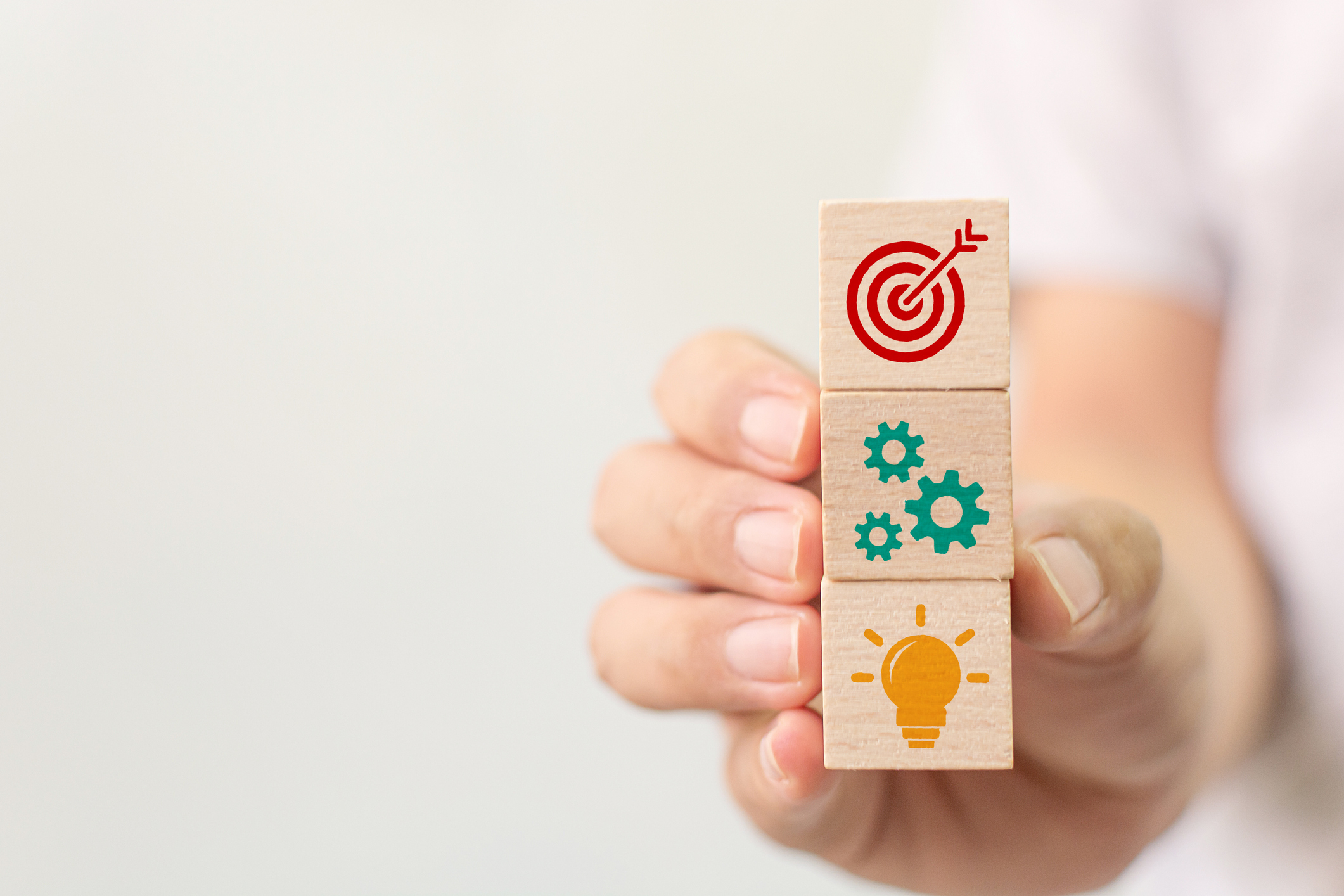 hand holding stack of wooden cubes with icons of target, gears and light bulb