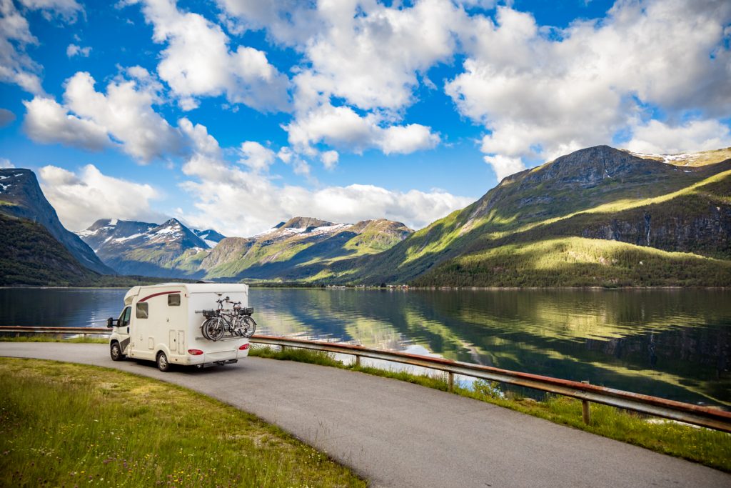 RV driving down scenic road beside lake