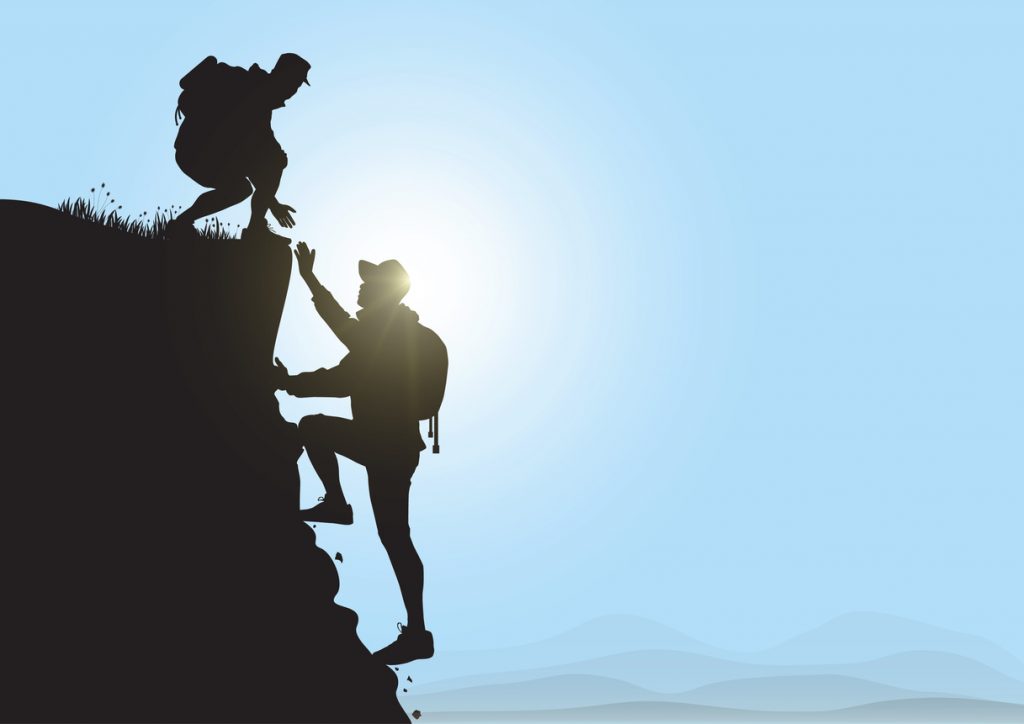 Silhouette of two people hiking climbing mountain and helping each other on blue sky