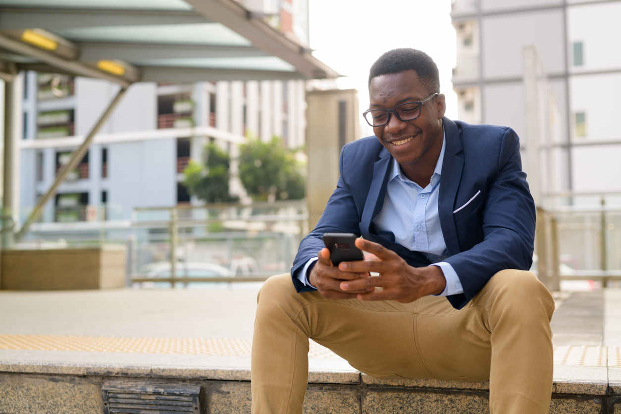 young man sitting outside train station looking at phone