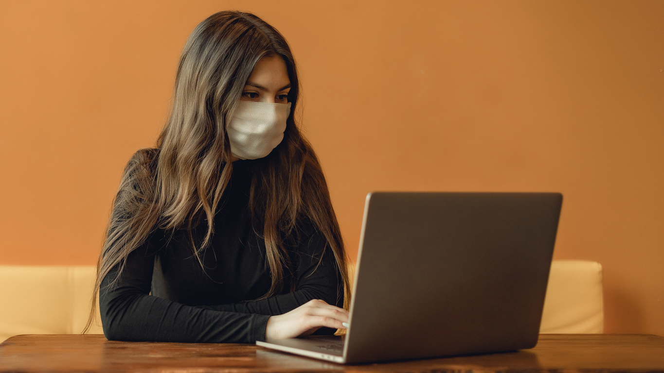 woman wearing face mask typing on laptop