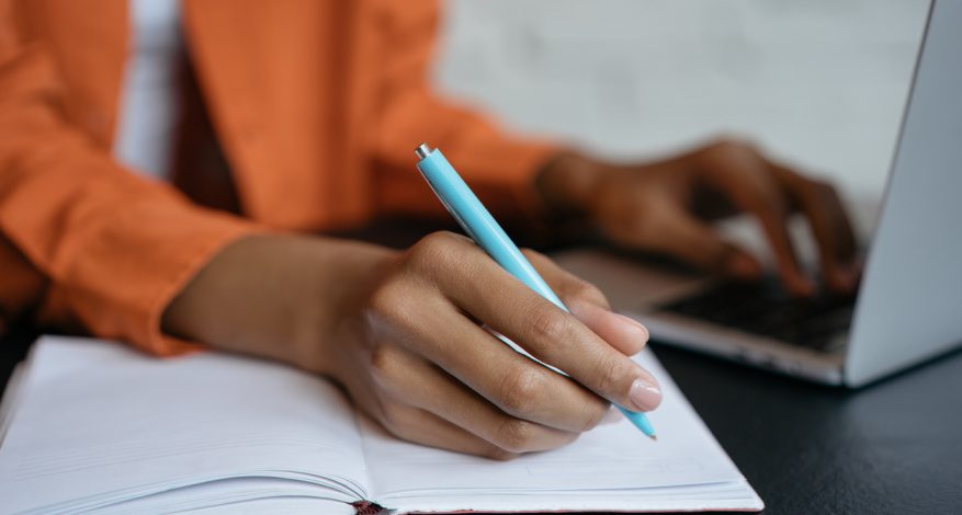 Close-up shot of hand holding pen and writing in noteboo