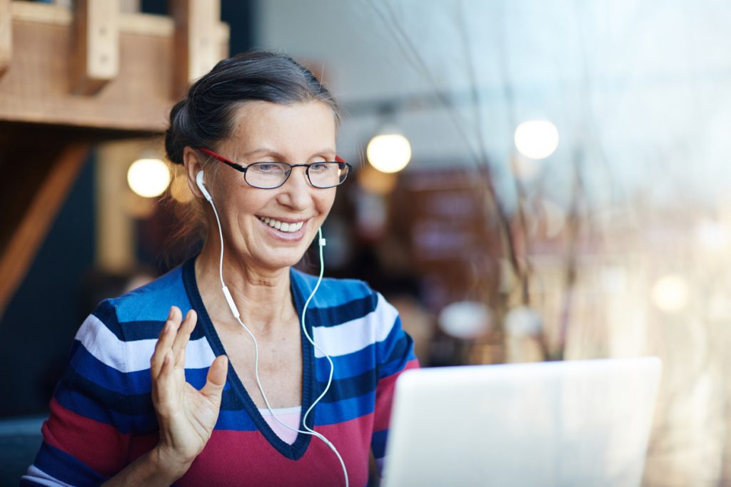 Woman wearing earphones and waving at computer screen.