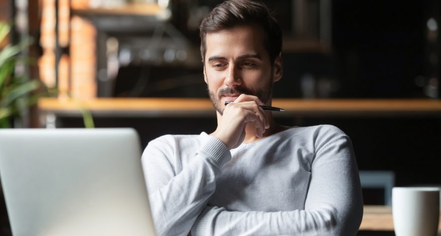 Man sitting at desk looking at laptop with pensive expression.