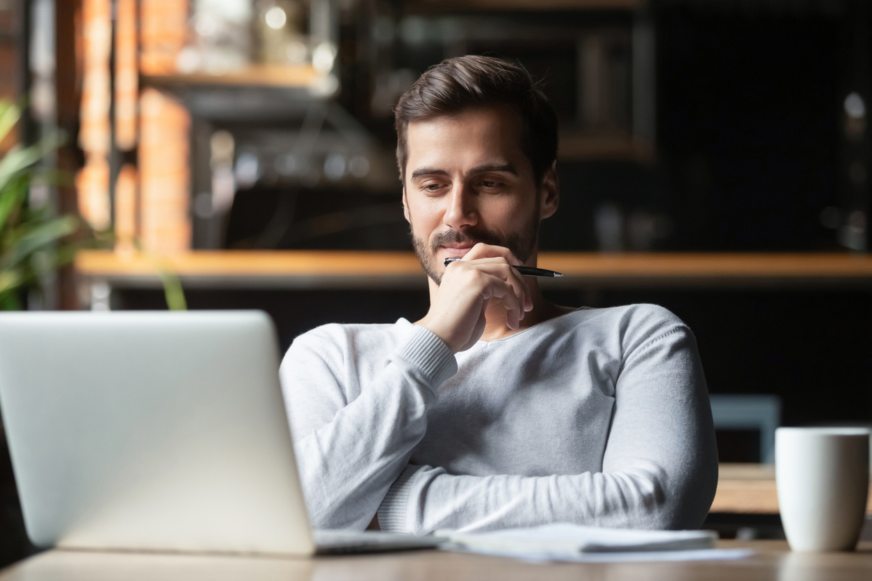 Man sitting at desk looking at laptop with pensive expression.