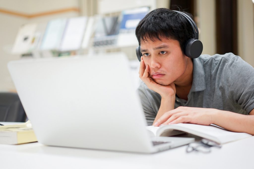 Male student resting head on hand looking at laptop