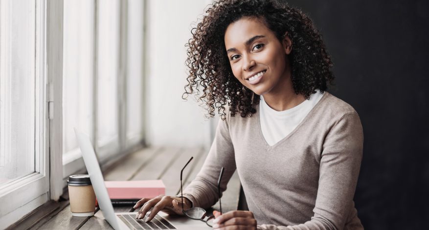 Woman smilingYoung woman student using laptop at cafe and taping at her computer