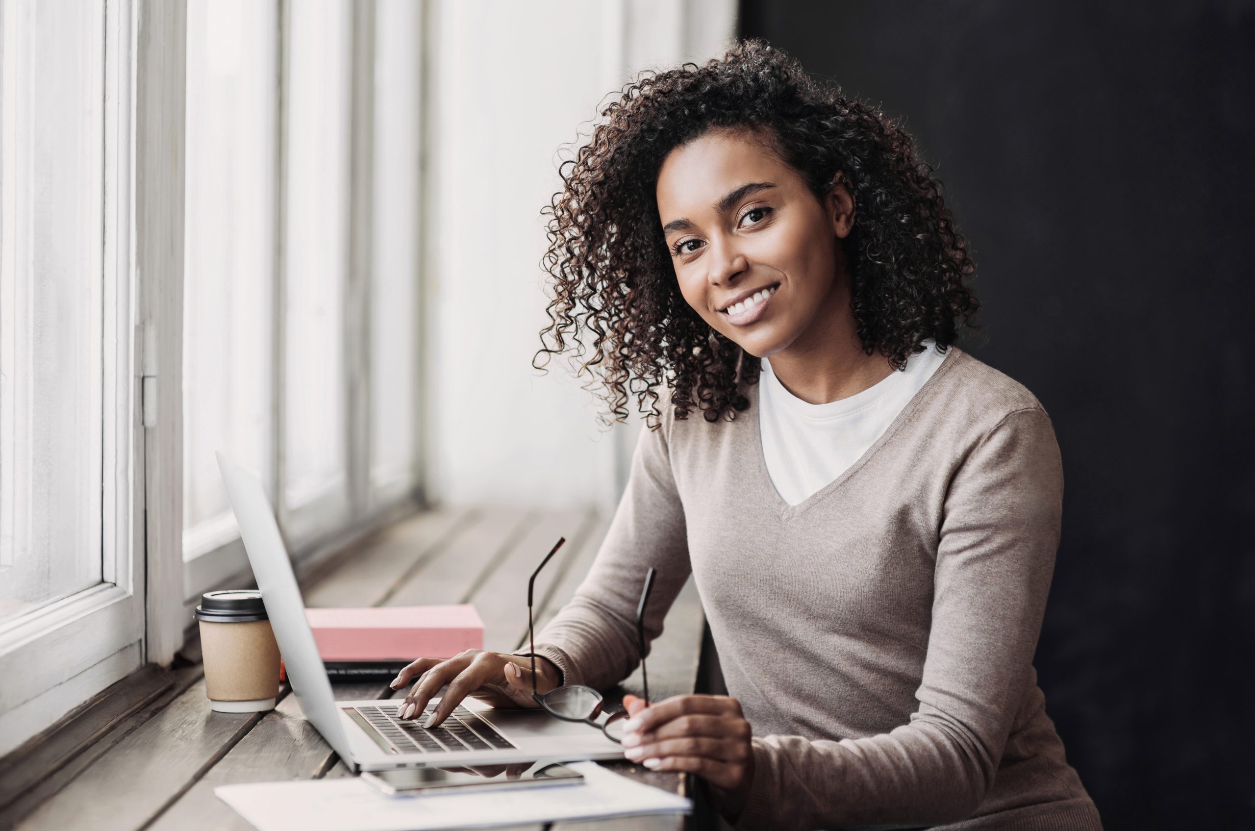 Woman smilingYoung woman student using laptop at cafe and taping at her computer