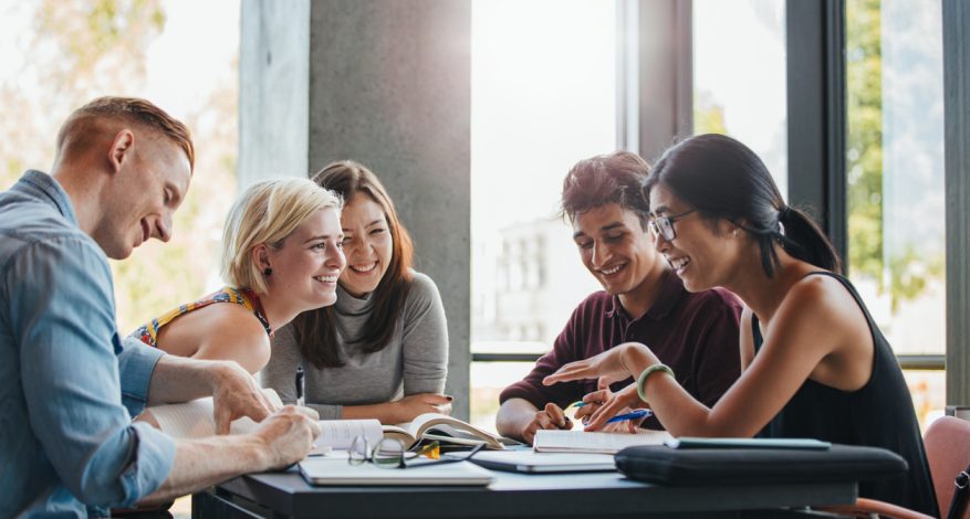 Happy group of university students studying with books in library