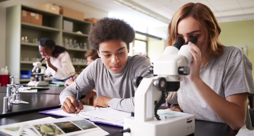 Two high school students looking through microscope in class