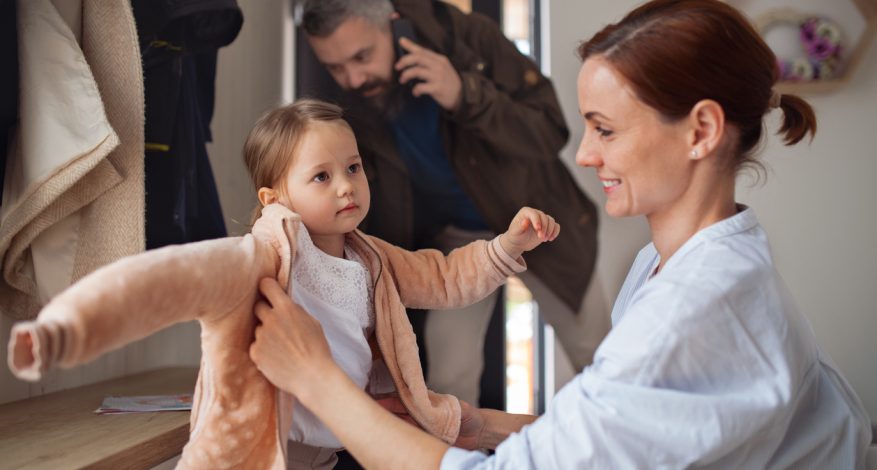 Busy father and mother with small daughter in entrance hall indoors in the morning, leaving for work and nursery school.