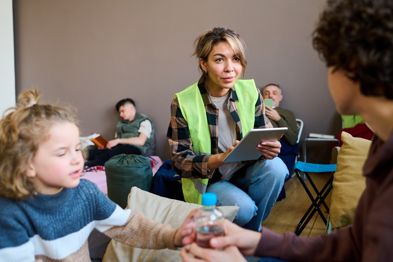 Young female volunteer with tablet squats in front of woman with son