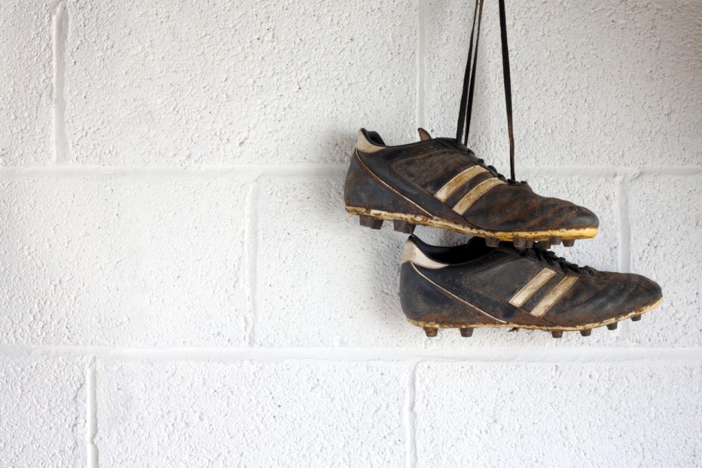 A pair of muddy black football boots hang up in a white-walled changing room.