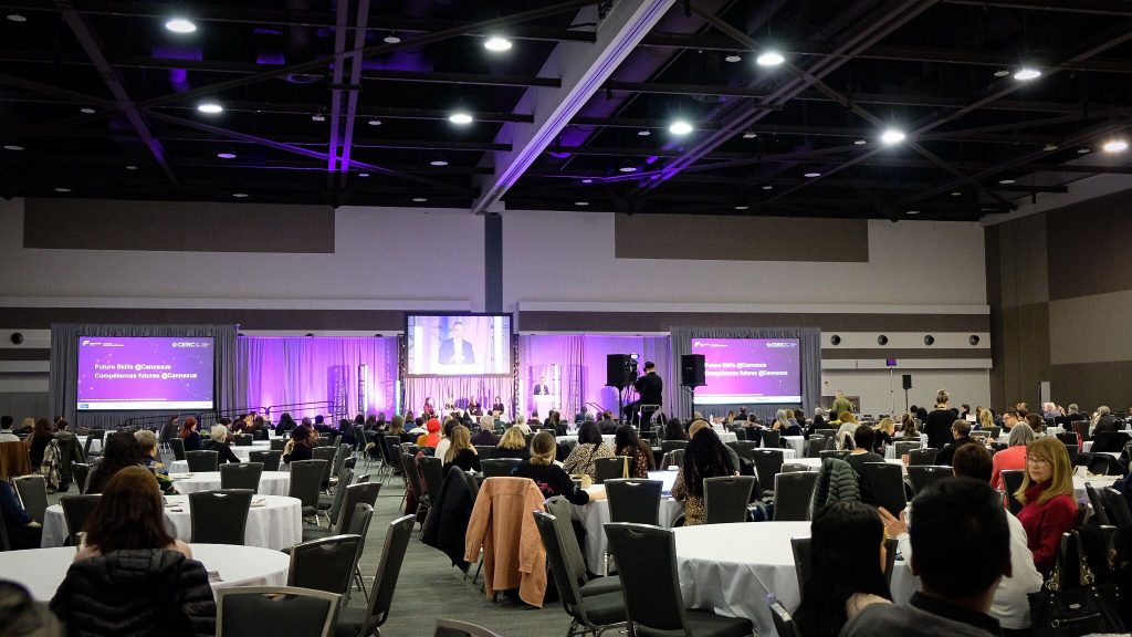 Delegates site at round tables listening to a speaker in the plenary hall at the Cannexus conference.