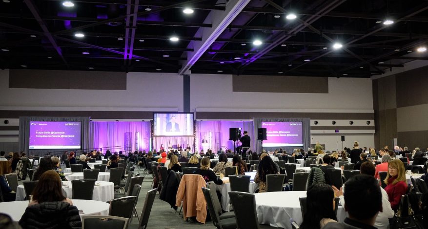 Delegates site at round tables listening to a speaker in the plenary hall at the Cannexus conference.