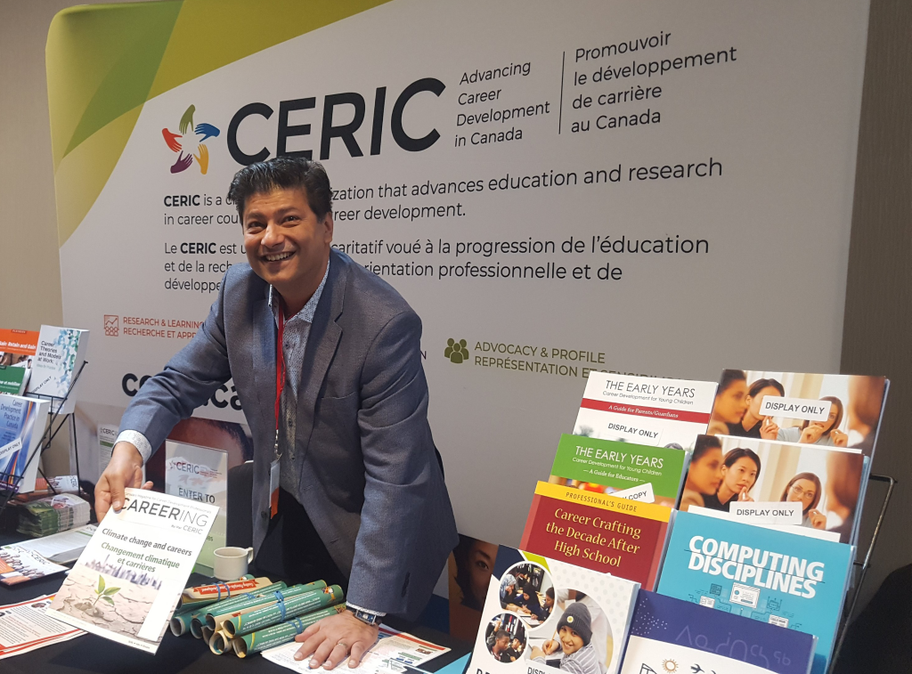 A smiling Riz Ibrahim shows off an issue of Careering magazine at the CERIC booth at a conference.