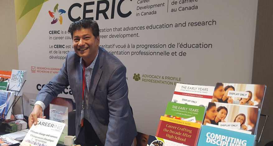 A smiling Riz Ibrahim shows off an issue of Careering magazine at the CERIC booth at a conference.